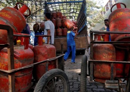Red domestic and blue commercial LPG gas cylinders with price drop alert tag in India